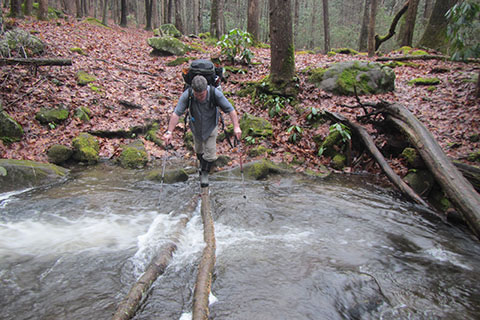 Backpacker crossing Greer Creek using a log as a bridge