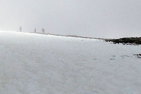 three hikers on the trail above the snow and in the clouds.