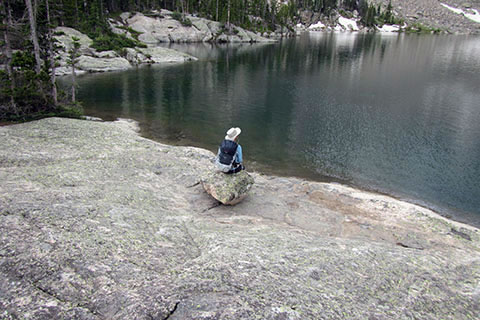 Hiker sitting on lone boulder overlooking lake